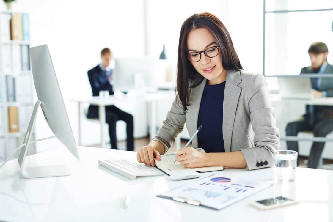 Woman working at a desk with charts and a computer in a bright office